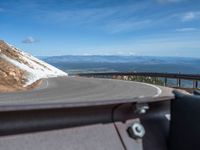 a man is riding his bike down a mountain road with snow and rocks in the background