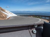 a man is riding his bike down a mountain road with snow and rocks in the background