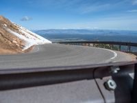 a man is riding his bike down a mountain road with snow and rocks in the background