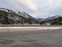 a street on the side of a snowy road in front of mountains with snow and trees