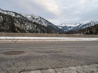 a street on the side of a snowy road in front of mountains with snow and trees