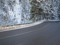 a paved roadway lined with trees covered in snow in the winter woods next to a mountain