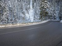 a paved roadway lined with trees covered in snow in the winter woods next to a mountain