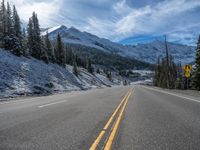 the empty road winds into a mountainous area with snow covered trees and mountains in the distance