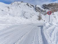 a person walks down a snowy road towards a mountain with a speed limit sign in front