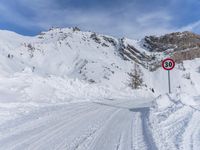 a person walks down a snowy road towards a mountain with a speed limit sign in front
