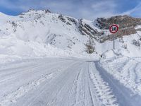 a person walks down a snowy road towards a mountain with a speed limit sign in front