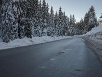 a snowy road next to evergreen trees on an icy day with blue sky and low clouds