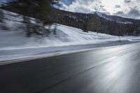 the front of a black car on a snowy road in front of mountains and clouds