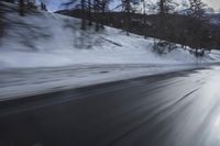 the front of a black car on a snowy road in front of mountains and clouds