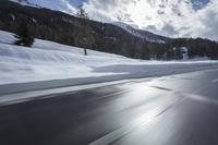 the front of a black car on a snowy road in front of mountains and clouds