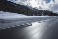 the front of a black car on a snowy road in front of mountains and clouds