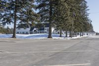 a road with parked cars and large evergreen trees on the roadside side of it is snow on the ground