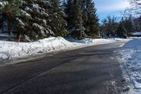 a road that has snow on the side and several trees by it along with blue sky in the background