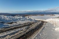 a snowy road lined with snow and rocks leading to mountains in the background, some have tire tracks