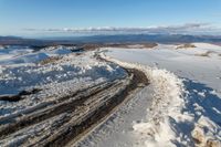 a snowy road lined with snow and rocks leading to mountains in the background, some have tire tracks