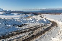 a snowy road lined with snow and rocks leading to mountains in the background, some have tire tracks