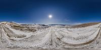 a snowy road surrounded by hills under a bright sun light and sky with snow on it