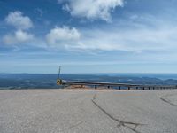 an empty road and a hill overlook the view of mountains and clouds and blue sky