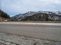 the roadway is wide and paved with many stone blocks in front of it there are several trees, a mountain and road in the background