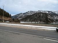 the roadway is wide and paved with many stone blocks in front of it there are several trees, a mountain and road in the background