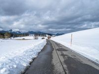 a snowy mountain side road with skis lined up along the sides and an ice - plowed driveway