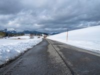 a snowy mountain side road with skis lined up along the sides and an ice - plowed driveway