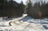 a stop sign stands on the side of a snowy road, as the sun shines