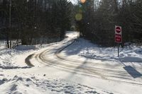 a stop sign stands on the side of a snowy road, as the sun shines