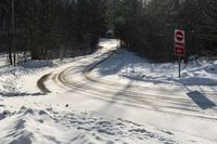 a stop sign stands on the side of a snowy road, as the sun shines