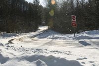 a stop sign stands on the side of a snowy road, as the sun shines