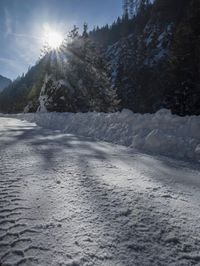 a snowy road covered in snow with trees behind it at sunset time, while the sun shines in a blue sky