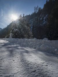 a snowy road covered in snow with trees behind it at sunset time, while the sun shines in a blue sky
