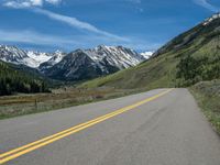 the road is paved with yellow markings and has a snowy mountain range in the background