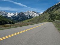 the road is paved with yellow markings and has a snowy mountain range in the background