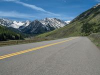 the road is paved with yellow markings and has a snowy mountain range in the background