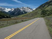 the road is paved with yellow markings and has a snowy mountain range in the background