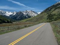 the road is paved with yellow markings and has a snowy mountain range in the background