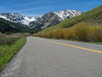 the road is paved with yellow markings and has a snowy mountain range in the background