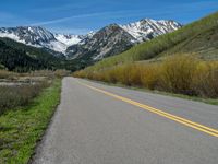 the road is paved with yellow markings and has a snowy mountain range in the background