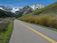 the road is paved with yellow markings and has a snowy mountain range in the background