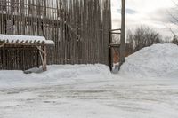 the snow is piled on the dirt next to the fence and building in the background