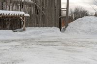 the snow is piled on the dirt next to the fence and building in the background