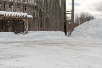 the snow is piled on the dirt next to the fence and building in the background