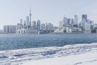 a person riding a bicycle on a snowy street near a city skyline with the ocean in front