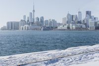 a person riding a bicycle on a snowy street near a city skyline with the ocean in front