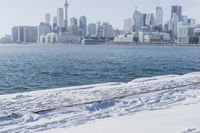 a person riding a bicycle on a snowy street near a city skyline with the ocean in front