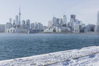 a person riding a bicycle on a snowy street near a city skyline with the ocean in front