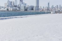 a person riding a bicycle on a snowy street near a city skyline with the ocean in front