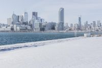 a person riding a bicycle on a snowy street near a city skyline with the ocean in front